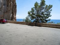 a red car parked near a cliff next to the ocean on a road side with blue skies