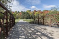 a wooden bridge over a paved path in the autumntime with fall foliage and a path winding through it