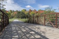 a wooden bridge over a paved path in the autumntime with fall foliage and a path winding through it