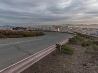 an empty street at dusk overlooking a city from a hill top bench with the sun peeking out