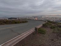 an empty street at dusk overlooking a city from a hill top bench with the sun peeking out