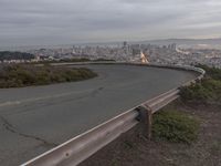 an empty street at dusk overlooking a city from a hill top bench with the sun peeking out