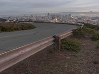 an empty street at dusk overlooking a city from a hill top bench with the sun peeking out