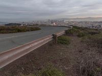 an empty street at dusk overlooking a city from a hill top bench with the sun peeking out