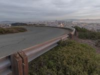 an empty street at dusk overlooking a city from a hill top bench with the sun peeking out