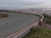 an empty street at dusk overlooking a city from a hill top bench with the sun peeking out