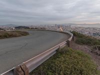 an empty street at dusk overlooking a city from a hill top bench with the sun peeking out