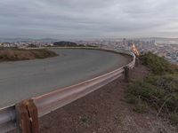 an empty street at dusk overlooking a city from a hill top bench with the sun peeking out