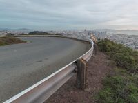 an empty street at dusk overlooking a city from a hill top bench with the sun peeking out