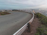 an empty street at dusk overlooking a city from a hill top bench with the sun peeking out