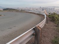 an empty street at dusk overlooking a city from a hill top bench with the sun peeking out