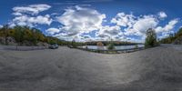 a panorama lens shot of the sky, trees, and a lake at the edge of a road