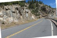 the winding highway is very steep and has a cliff side, with pine trees on each side