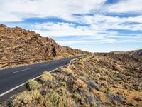 a long, narrow road leading to rocks and a rocky hillside at the desert landscape