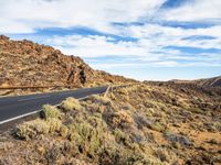 a long, narrow road leading to rocks and a rocky hillside at the desert landscape