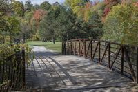 a wooden bridge over a paved path in the autumntime with fall foliage and a path winding through it