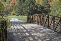 a wooden bridge over a paved path in the autumntime with fall foliage and a path winding through it