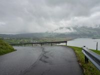 a winding road with a bridge on the side of it surrounded by mountains and water