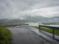 a winding road with a bridge on the side of it surrounded by mountains and water