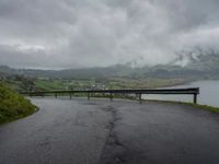 a winding road with a bridge on the side of it surrounded by mountains and water