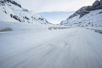 the car travels along the mountainous road on snowy day - like terrain, driving through snow - covered mountains and forest