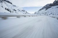 the car travels along the mountainous road on snowy day - like terrain, driving through snow - covered mountains and forest