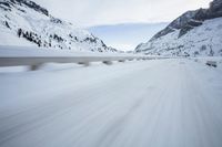 the car travels along the mountainous road on snowy day - like terrain, driving through snow - covered mountains and forest