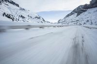 the car travels along the mountainous road on snowy day - like terrain, driving through snow - covered mountains and forest
