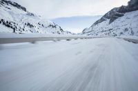 the car travels along the mountainous road on snowy day - like terrain, driving through snow - covered mountains and forest