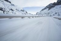 the car travels along the mountainous road on snowy day - like terrain, driving through snow - covered mountains and forest