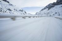 the car travels along the mountainous road on snowy day - like terrain, driving through snow - covered mountains and forest