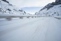 the car travels along the mountainous road on snowy day - like terrain, driving through snow - covered mountains and forest