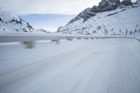 the car travels along the mountainous road on snowy day - like terrain, driving through snow - covered mountains and forest