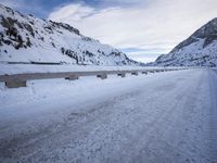 a narrow dirt road surrounded by snow covered mountains under a blue sky and clouds are visible
