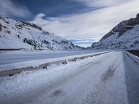 a narrow dirt road surrounded by snow covered mountains under a blue sky and clouds are visible