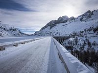 a narrow dirt road surrounded by snow covered mountains under a blue sky and clouds are visible