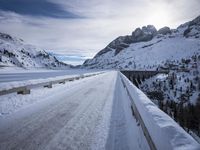 a narrow dirt road surrounded by snow covered mountains under a blue sky and clouds are visible