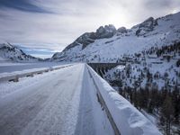 a narrow dirt road surrounded by snow covered mountains under a blue sky and clouds are visible