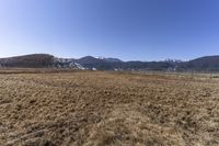 the field that is in front of a fence and mountains with brown grass around it