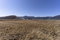 the field that is in front of a fence and mountains with brown grass around it