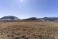 the field that is in front of a fence and mountains with brown grass around it