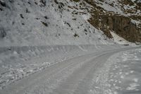 a snow covered road going past a cliff on the side of a mountain with tracks in it