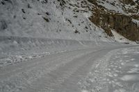 a snow covered road going past a cliff on the side of a mountain with tracks in it