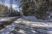 snow covered country road on a sunny day with a lot of trees and bushes around it