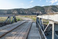 a lone man on a bridge, near a dirt path, and mountains, overlooking