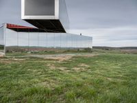 an empty glass building sits on top of grass near a field of dead grass and hills