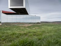 an empty glass building sits on top of grass near a field of dead grass and hills