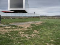 an empty glass building sits on top of grass near a field of dead grass and hills