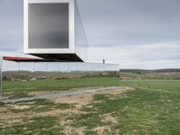 an empty glass building sits on top of grass near a field of dead grass and hills