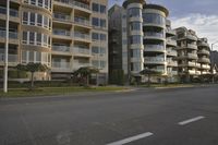 an empty intersection with a large apartment complex behind it and a man riding a skateboard on the other side